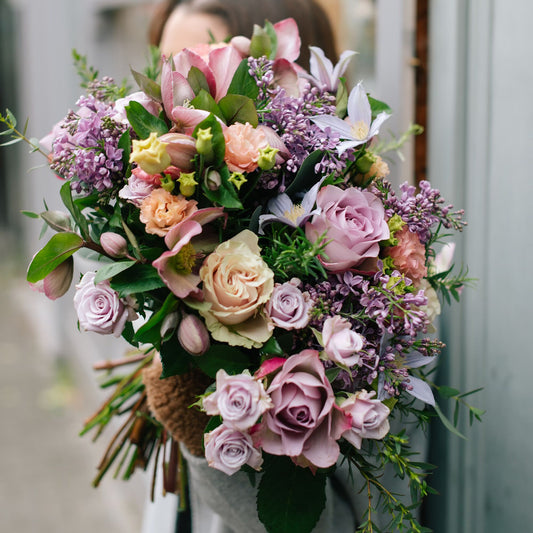 A beautiful bouquet of flowers in shades of lilac, pink, cream, and yellow. This stunning arrangement includes a blend of roses, clematis, populus, hellebore, and lisianthus, expertly hand-selected and arranged by our florists. The vibrant colors and elegant design make it perfect for any occasion.